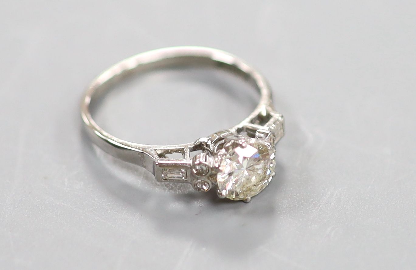 A white metal(stamped platinum) and single stone diamond ring with baguette and round cut diamond set shoulders